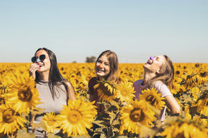 Three girls in a field of sunflowers, wearing Nöz's colorful, eco friendly sunscreen.